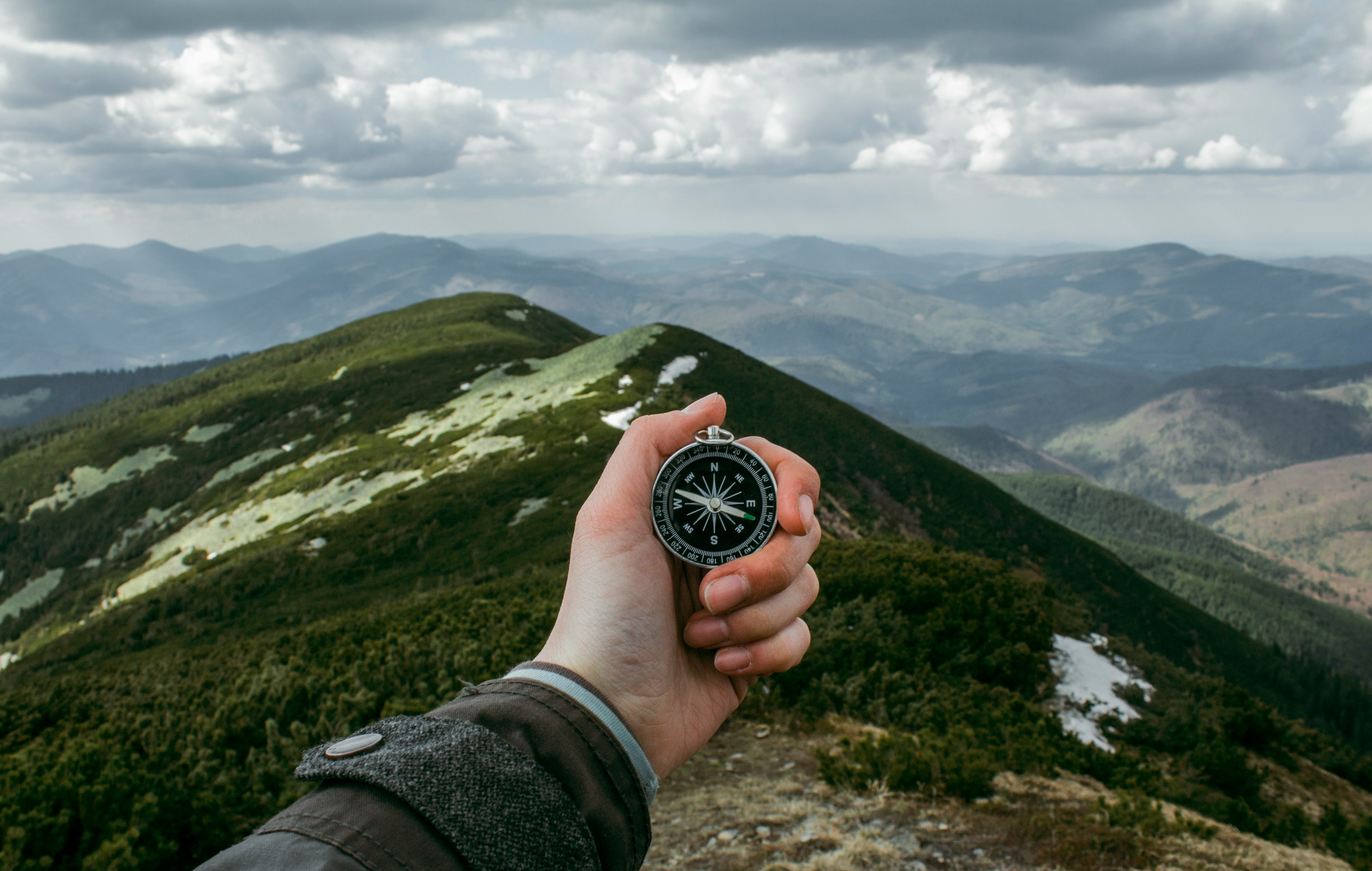 Hand holding a compass overlooking a mountain landscape, representing strategic direction